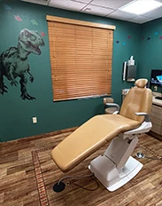 Pediatric dental exam room with dinosaur mural and exam chair