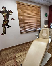 Superhero-themed pediatric dental exam room with tan chair and wall decals